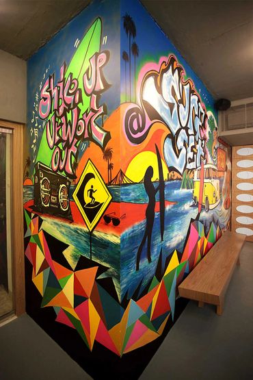 Colorful surf-themed graffiti mural on a corner wall with vibrant geometric patterns.