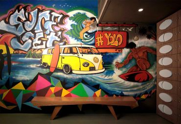 Colorful surf-themed mural with surfers, a yellow VW van, and #YOLO text.