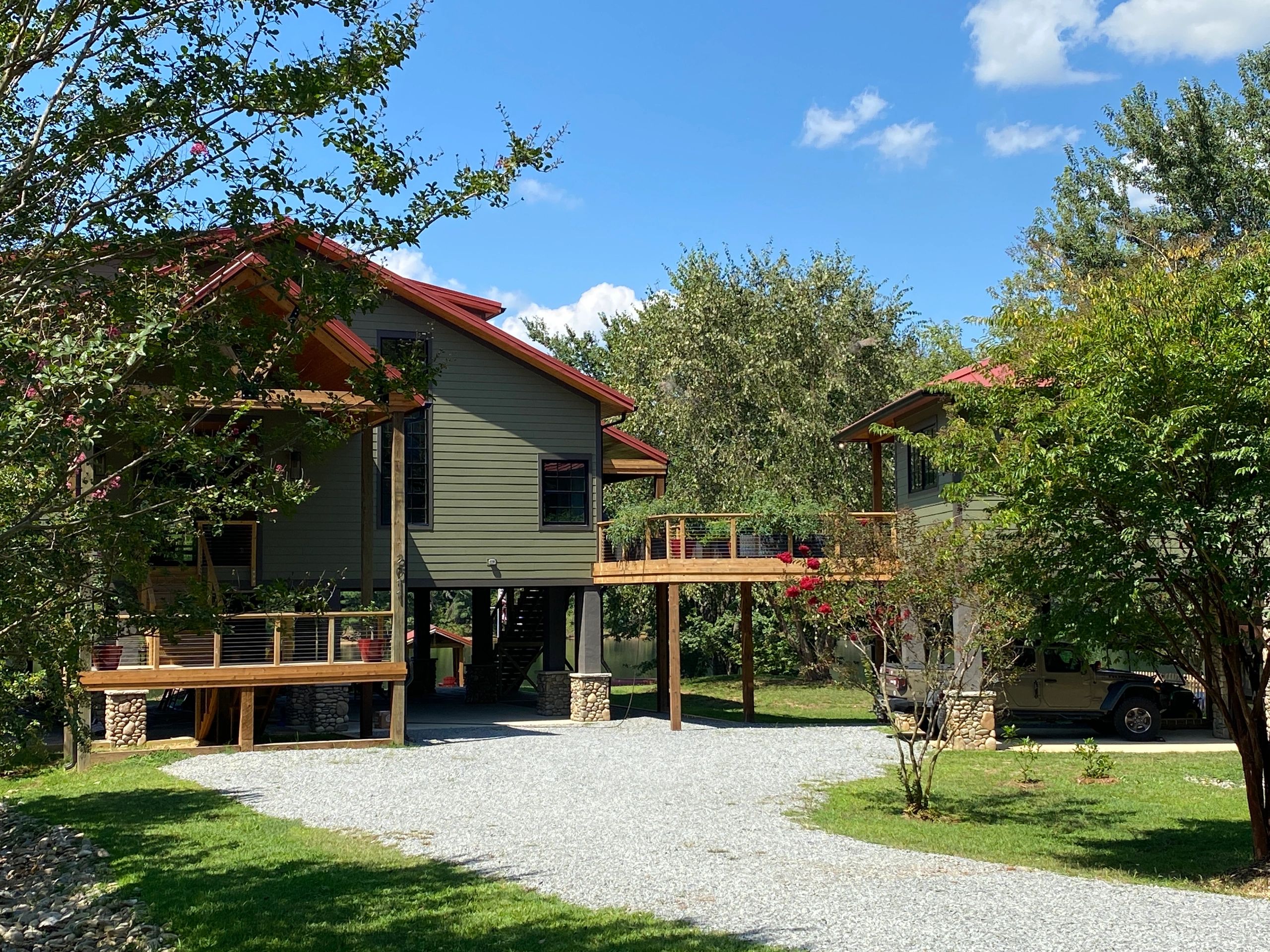 Two elevated houses connected by a wooden bridge in a green, sunny setting.