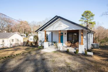 Cozy white house with a blue door and wooden porch pillars.
