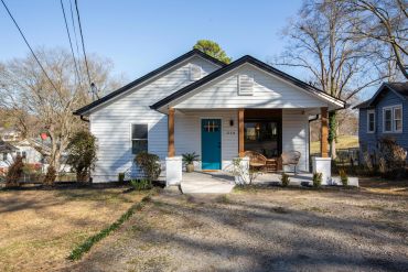 A charming white house with a turquoise door and wooden porch columns.