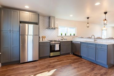 Modern kitchen with blue cabinets, stainless steel appliances, and wooden flooring.