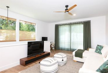 Bright modern living room with white sofa, poufs, and wooden TV stand.