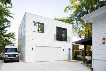 Modern white two-story garage with black-framed windows and a parked white Mercedes van.