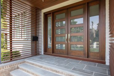 Modern wooden double front doors with glass panels and horizontal wooden slats on the side.