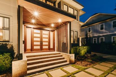 Modern house entrance with wooden double doors illuminated at night.