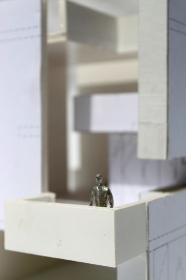 A miniature metallic figure on a white architectural model balcony.