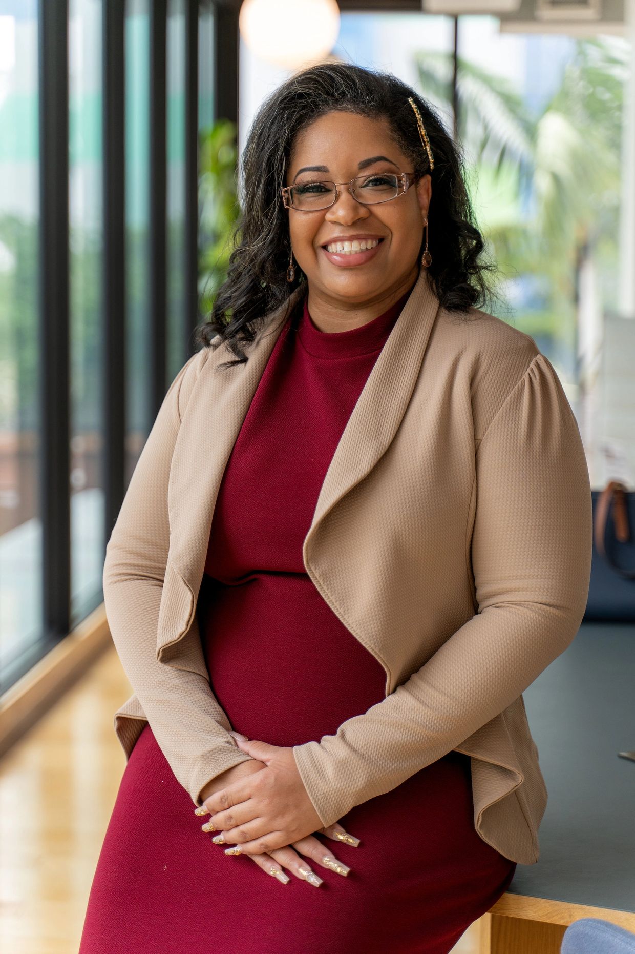 Woman sitting on table dressed in business attire and smiling.
