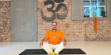 yoga stüdyosunda kelebek pozu yapan bir yogi ve duvarda Sanskrit dilinde OM