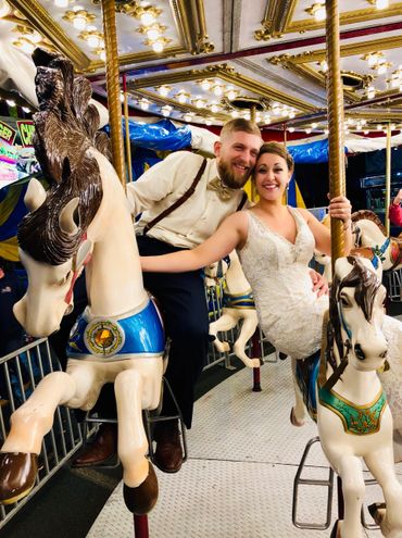 Happy couple in wedding attire enjoying a carousel ride together.