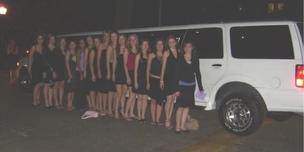 A group of young women lined up beside a white limousine at night.