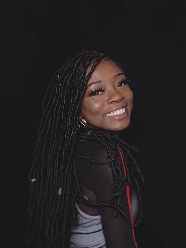 Smiling woman with long dreadlocks against a black background.