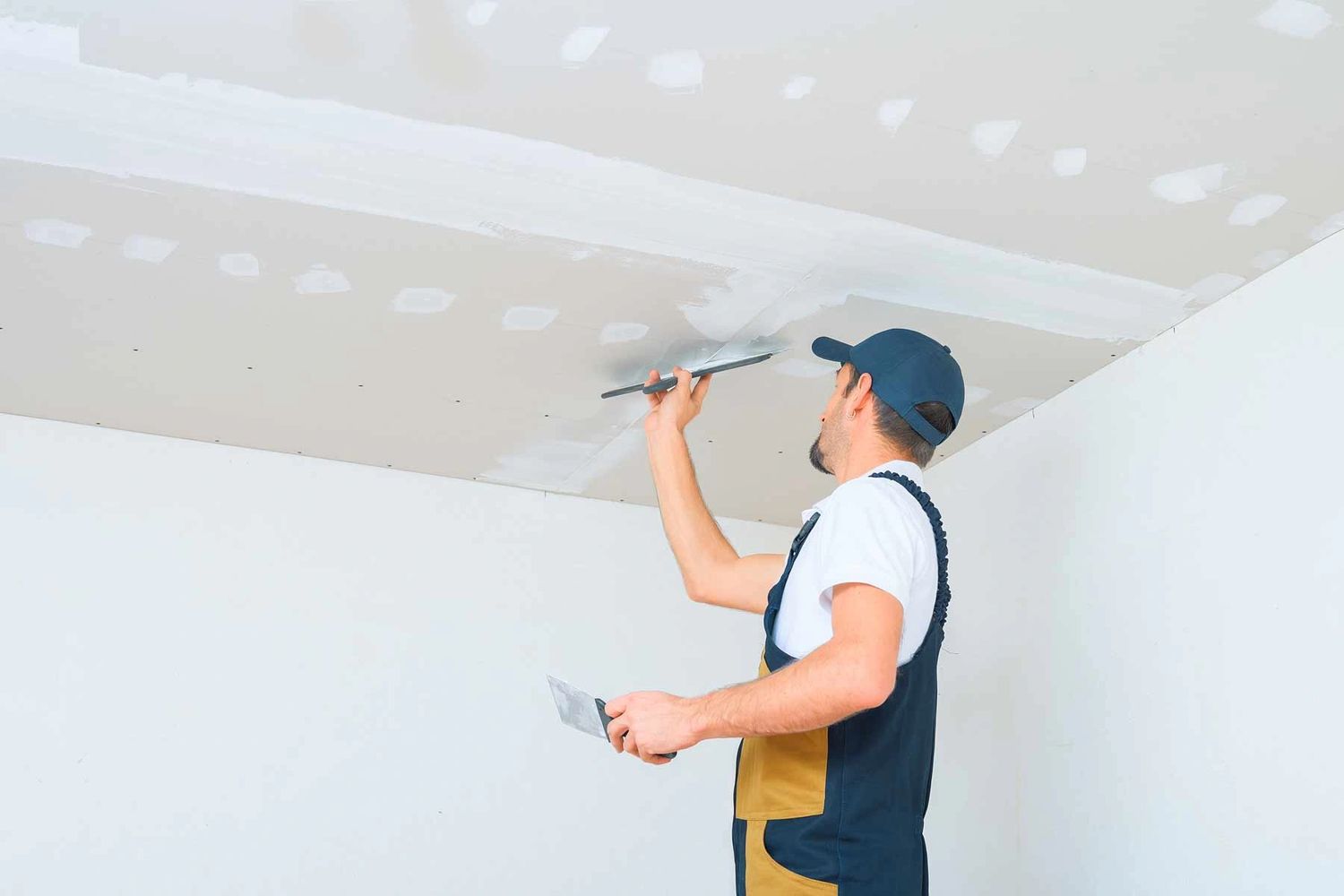 Worker applying plaster on ceiling drywall seams.