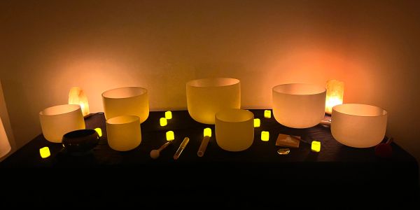 Glowing sound bowls and candles on a dark table.