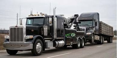 A tow truck towing a large semi-truck on a highway.