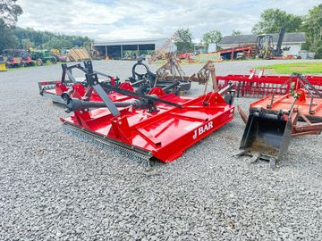 Red J Bar rotary mower on gravel with farming equipment around.