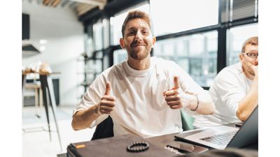 Man giving a thumbs-up while sitting at a desk with a laptop.