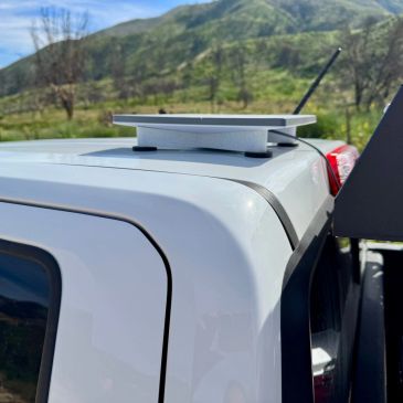 White device mounted on a vehicle roof with mountainous background.