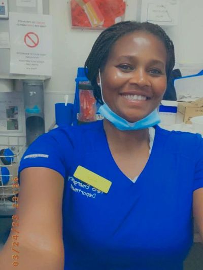 A smiling healthcare worker in blue scrubs with a mask under her chin.