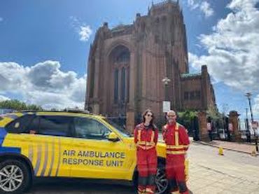Air ambulance response unit members stand beside their vehicle outside a historic building.