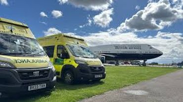 Two ambulances parked near a large airplane on a sunny day.
