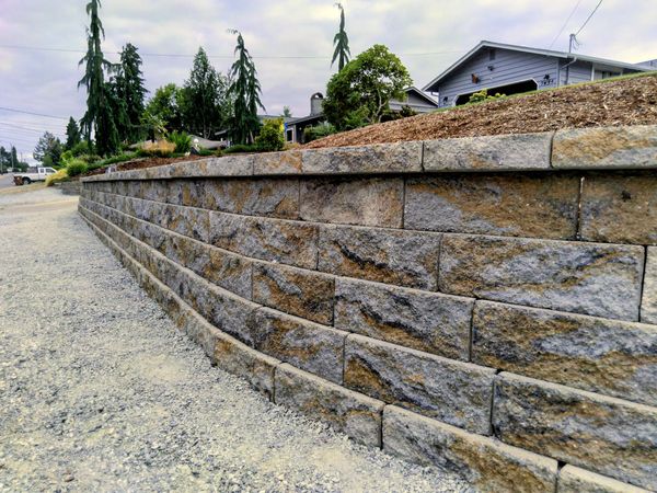 Stone retaining wall with landscaping and houses in the background.