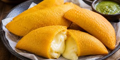 Golden fried cheese-filled empanadas served with green sauce.
