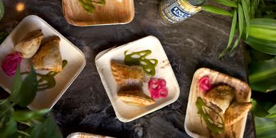 Plates of samosas with green chutney and pink pickled onions on a dark table.