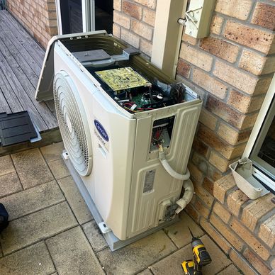 Open Carrier inverter AC unit with tools outside a brick house.