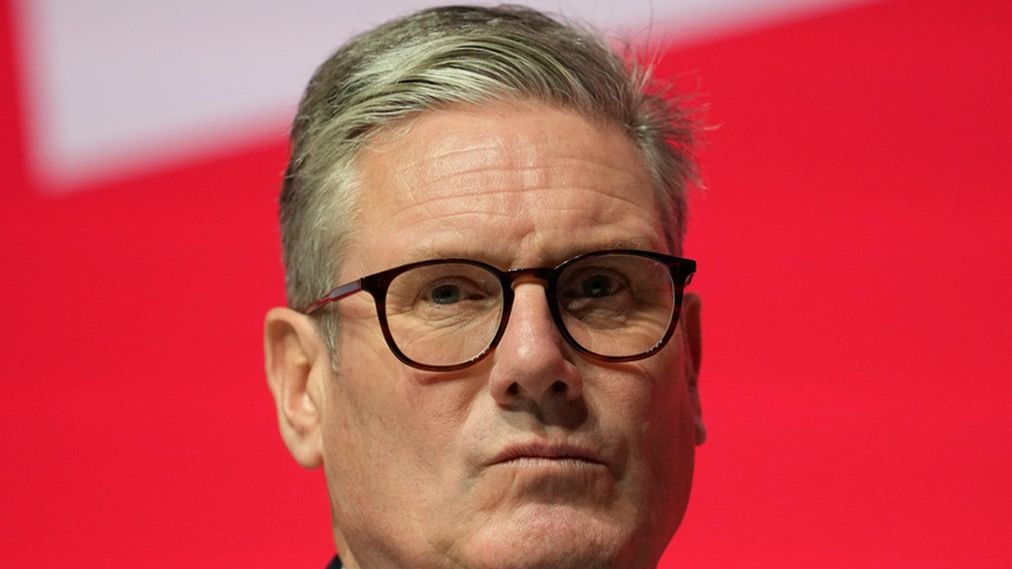 Close-up of a serious man wearing glasses against a red background.