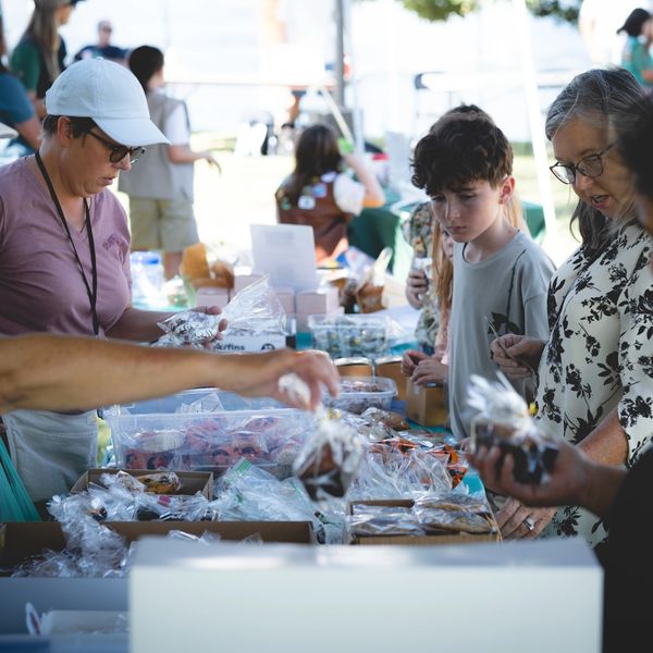 People browsing a table of baked goods at an outdoor market.