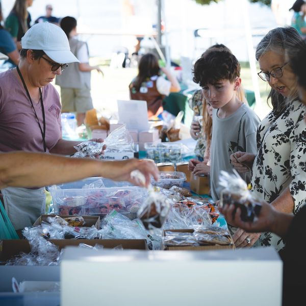 People browsing a table of baked goods at an outdoor market.