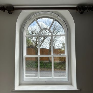 Arched window with a view of trees and a fence.