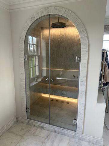 Modern glass shower with arched entrance and bench.