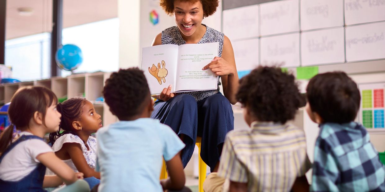A female teacher reads to elementary school students  sitting on floor in class at school