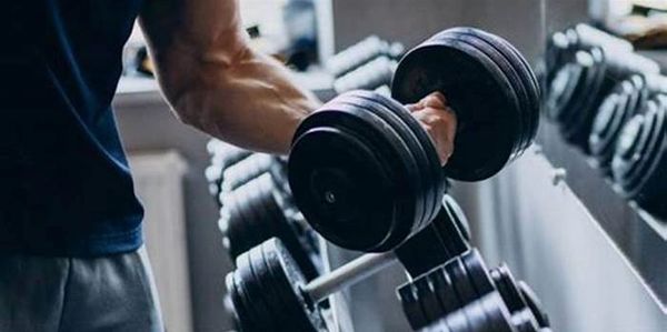 Person lifting a heavy dumbbell in a gym setting.