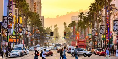 Busy Hollywood street at sunset with people crossing and heavy traffic.