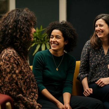 Three women engaged in a joyful conversation, smiling and laughing together.