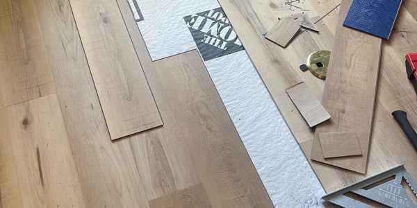 Flooring installation in progress with wooden planks and tools scattered.