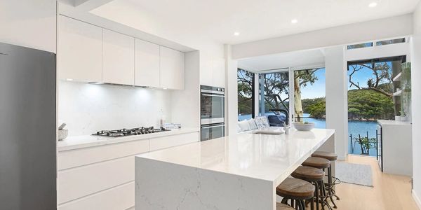 Modern white kitchen with white marbled stone island and white cabinetry looking out to water views 