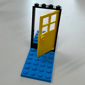 A yellow LEGO door attached to a black frame on a blue baseplate.
