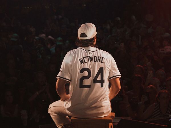 Person wearing a Wetmore 24 jersey sits on a stool facing a crowd.