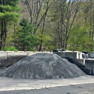 Pile of gravel in an outdoor storage area surrounded by trees.