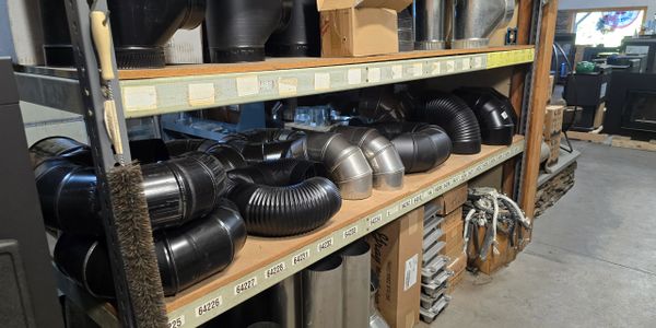 Shelves filled with various black and metal duct pipes in a workshop.