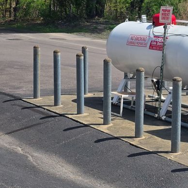 Gas tank protected by metal bollards in an outdoor area.