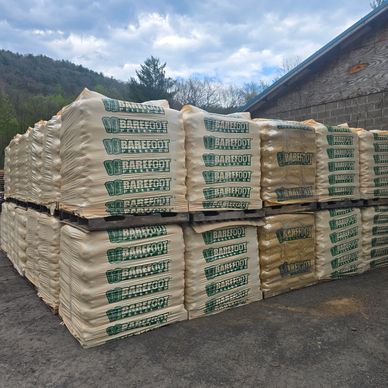 Stacks of Barefoot brand fertilizer bags outdoors near a building.