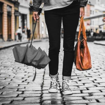 A person standing on the road by holding umbrella and bag