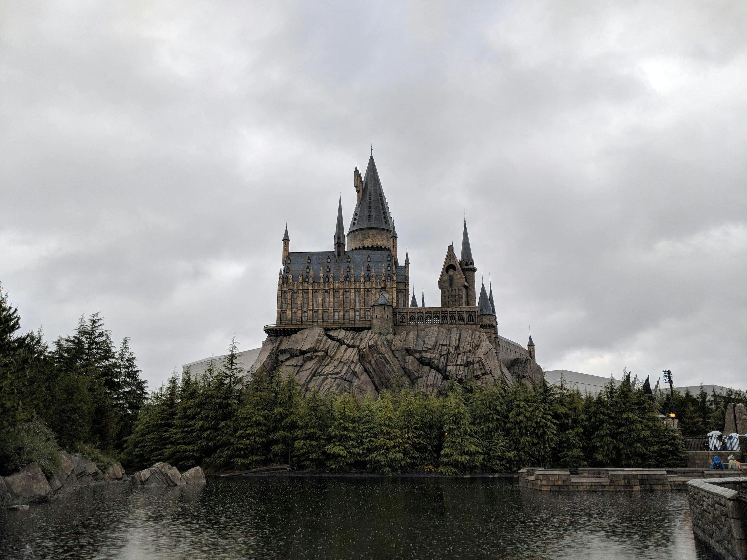 Hogwarts castle replica surrounded by trees and water under a cloudy sky.