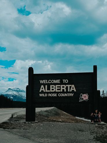Wilder, Noah and Adalaide standing in  front of the Alberta provincial boarder sign between BC & AB.