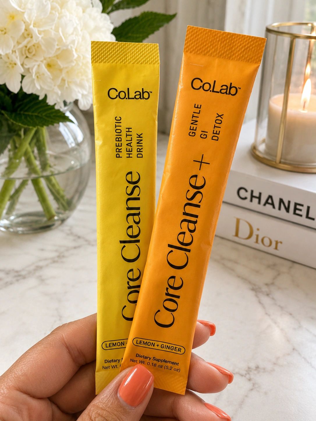 Hand holding two Co.Lab Core Cleanse packets in yellow and orange.